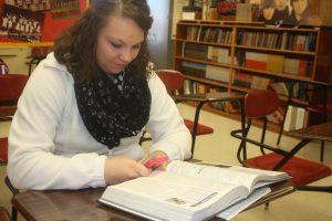 Brianna R. Dunkle texts druing a requred class with her book open in front of her.