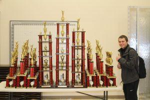 Nathan Baldwin, senior, standing next to all of he trophies for the Masquerade this weekend.