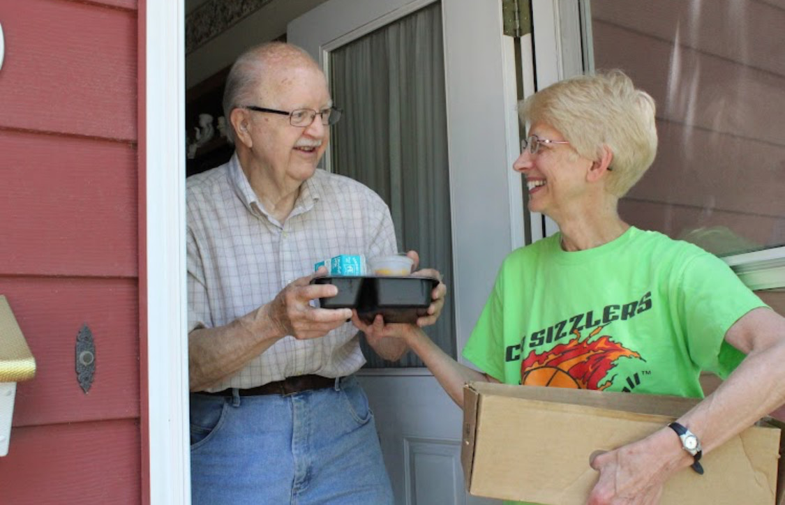 Meals on Wheels driver happily delivers a hot meal to a grateful client. 