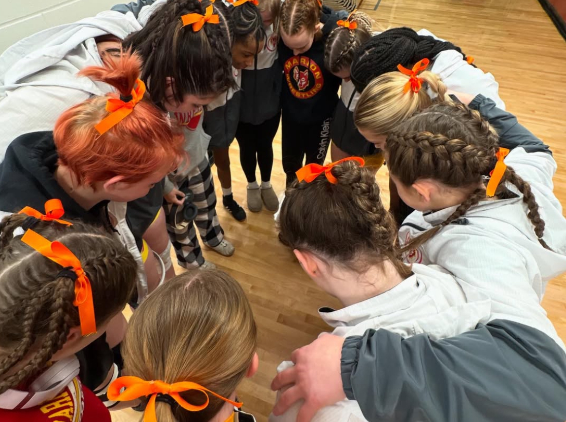 The girls wrestling team engages in a team huddle at Regionals. This tournament ended an era for some and opened new doors for others.