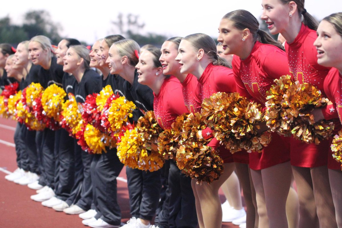 The poms and cheer teams interlock arms at a home football game, chanting their classic “Go’ Fight’ Win!” cheer. 