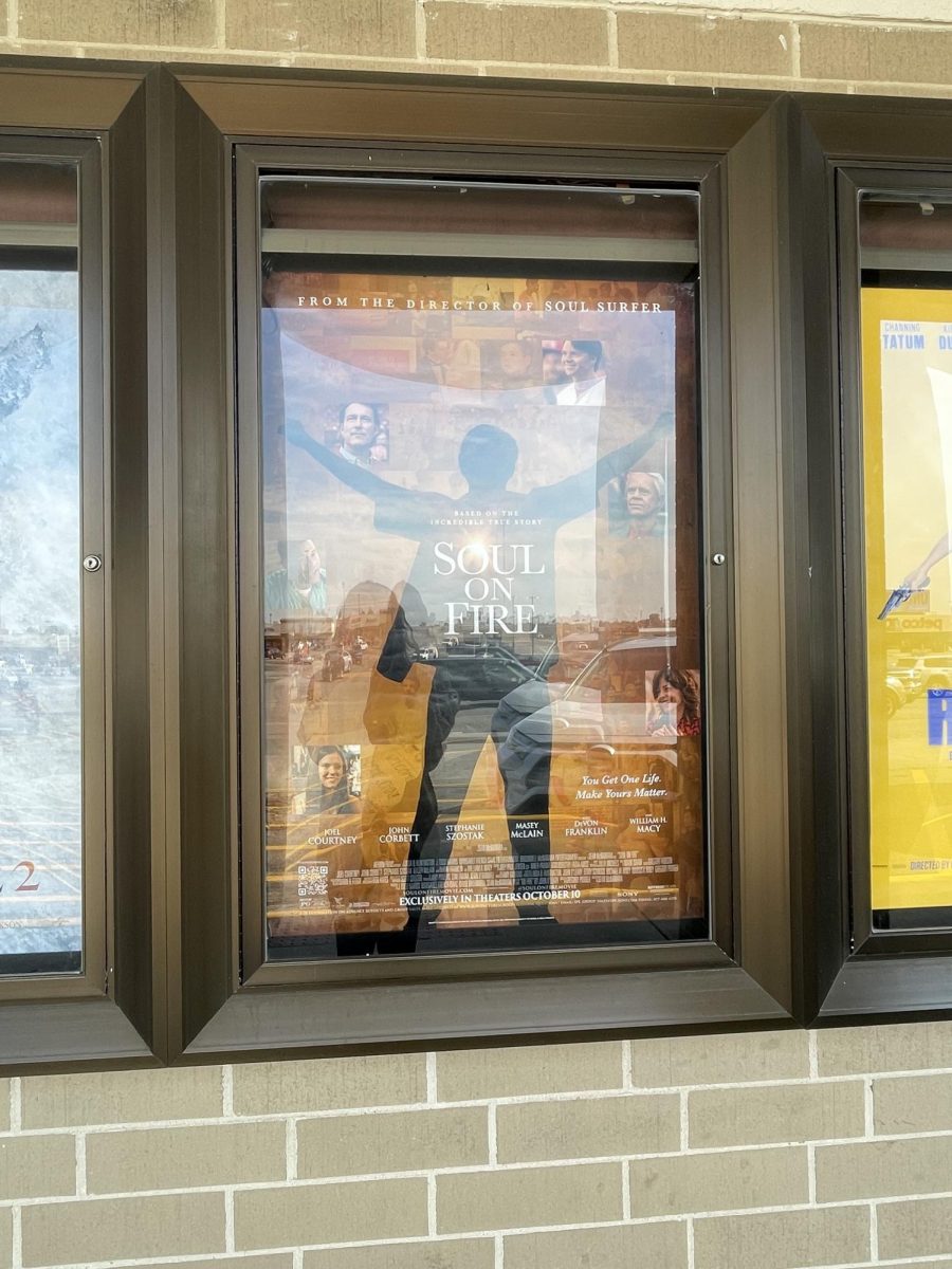 A movie poster shows young John O’Leary standing with arms out in accomplishment alongside the people who most influenced his journey positively.  