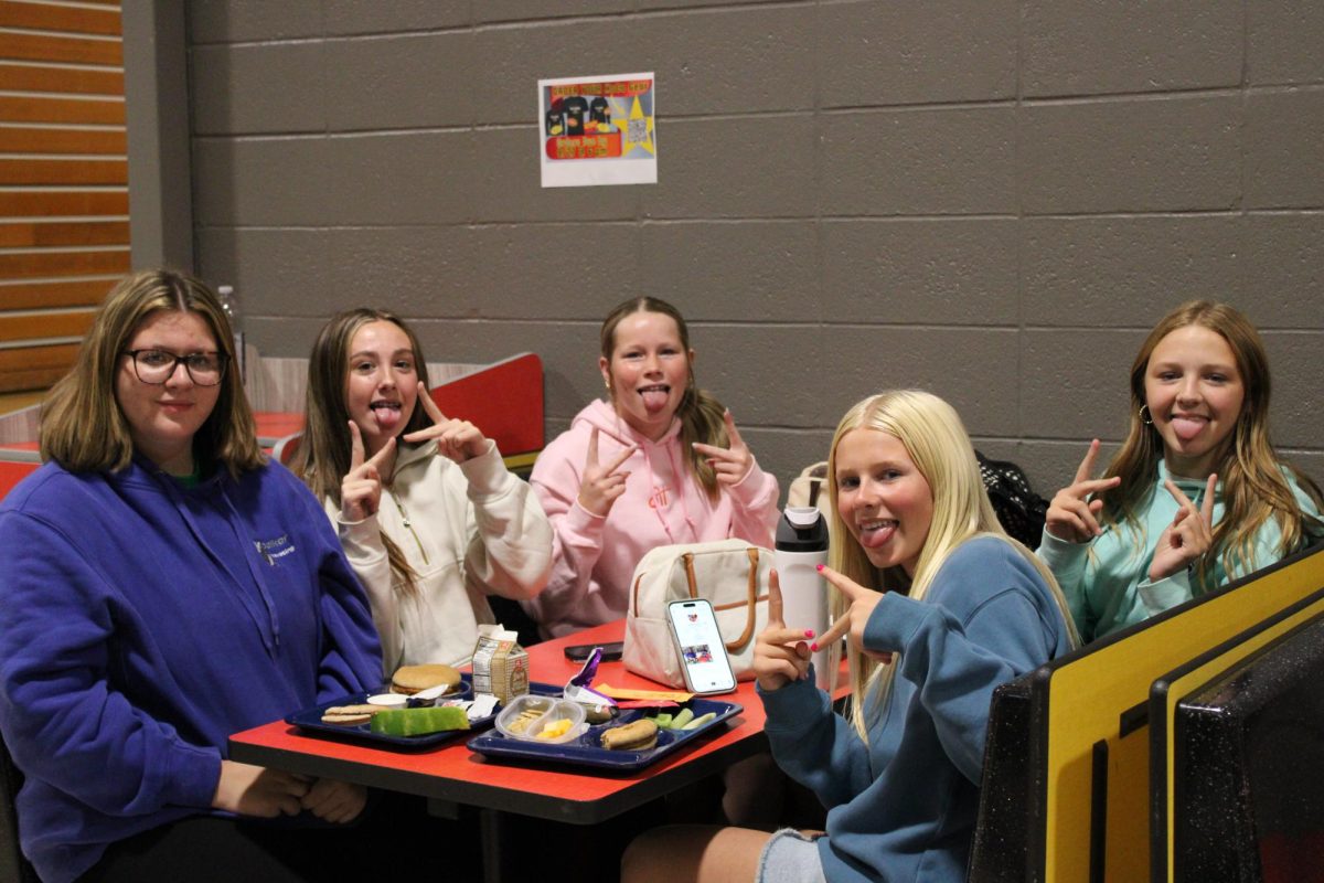 A group of freshmen girls poses happily at lunch, getting their photo taken. All with positive stories and passion coming together to enjoy a meal.