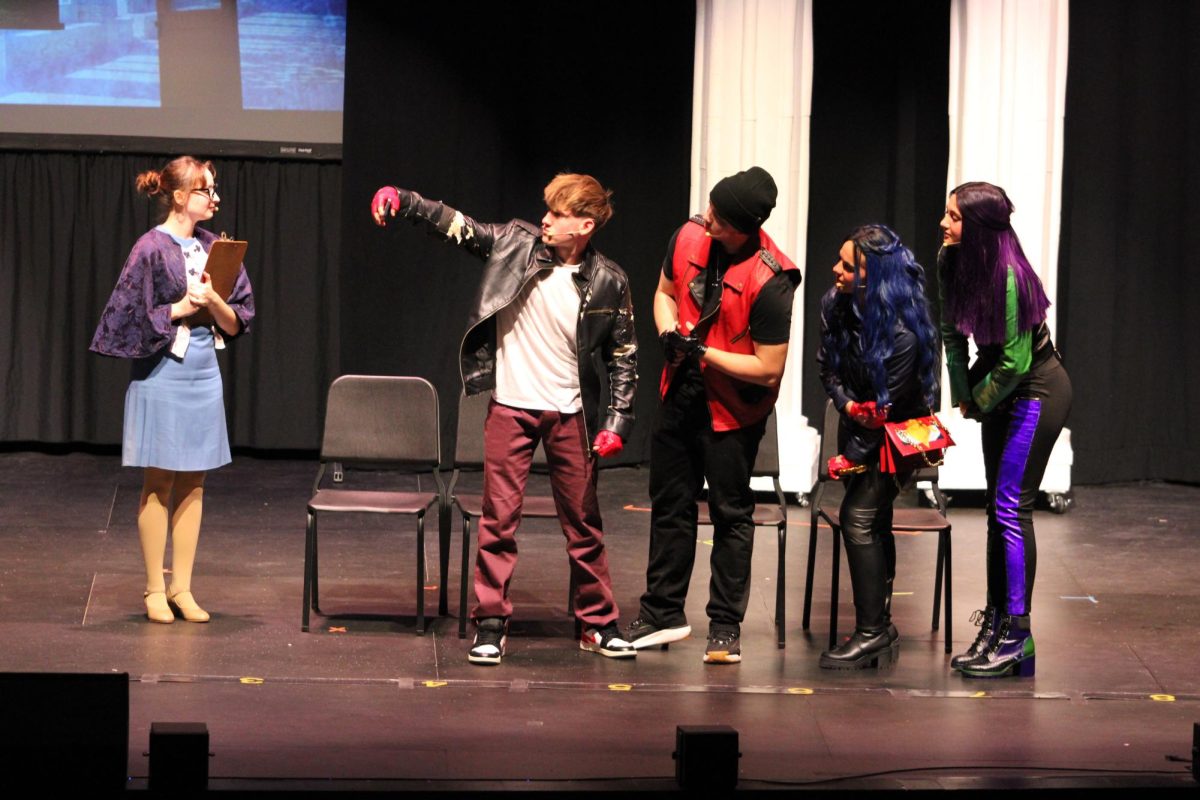The Villain Kids (Connor Bussey, Logan Ficek, Mady Fentree, and Alana Dyrland) FaceTime their villain parents while Fairy Godmother (Abby Andreasen) looks on during the spring musical, "Descendants."
